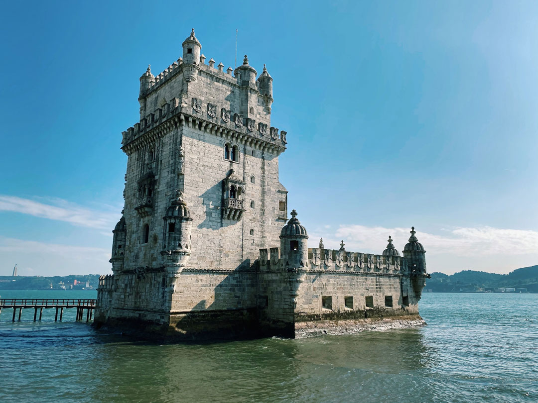 An abandon European Old Castle in the middle of the sea, where's there's a bridge connected, with blue sky white clouds as background. At the far horizon, there are sighting of modern township